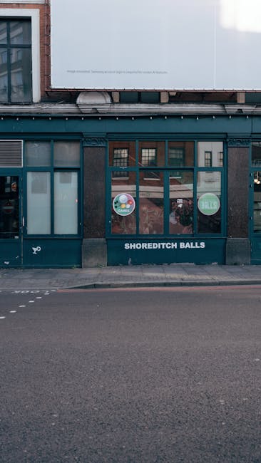 The storefront features a dark teal-painted wooden exterior with multiple glass windows and a glass door, displaying circular decals with colorful graphics and text on the entrance. Below the door, th